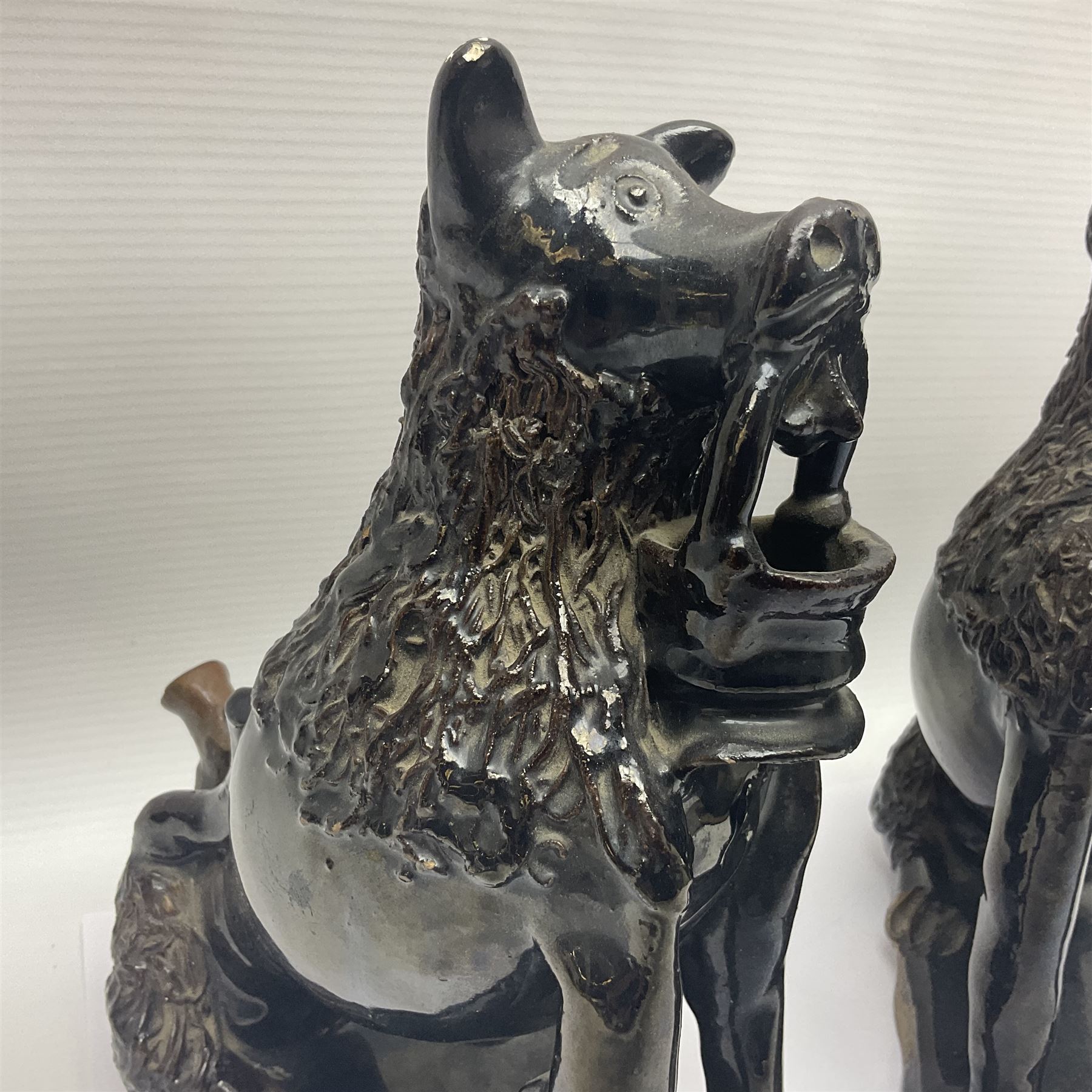 Pair of unusual early English pottery figures, modelled in the form of seated dogs with baskets between their jaws, the tails forming whistles, each upon rectangular base, overall H22cm