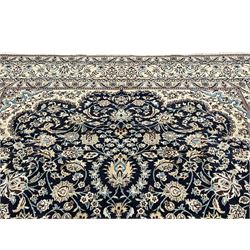 Persian Kashan indigo ground carpet, the central ivory rosette medallion surrounded by trailing and interlaced flower heads and branches, matching spandrels with floral design, the border with scrolling pattern decorated with stylised plant motifs within guards