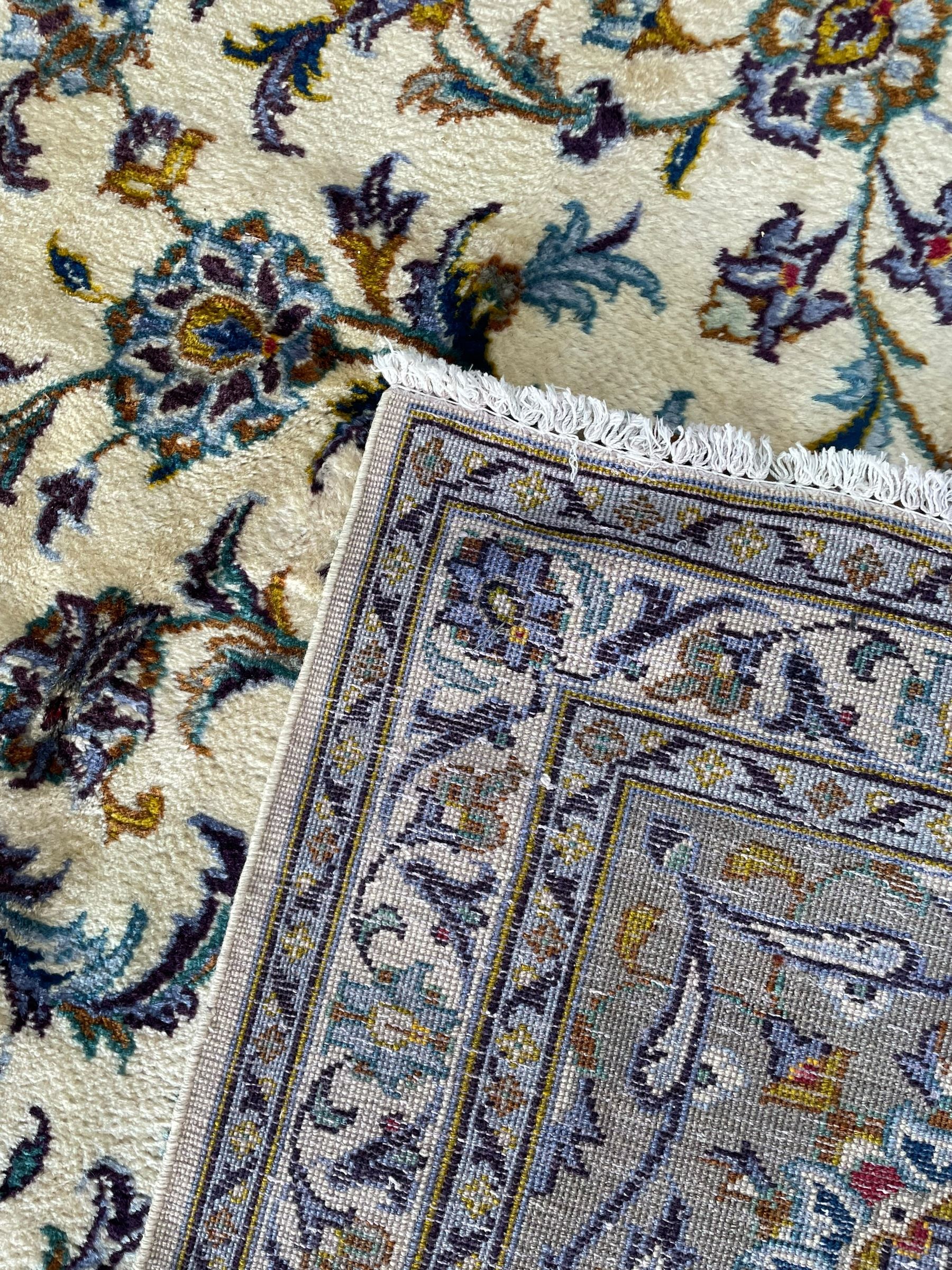 Persian Kashan ivory ground carpet, the busy field decorated with scrolling and interlaced leafy branches and palmettes, trailing branch border with repeating stylised plant motifs, within floral pattern guard stripes 