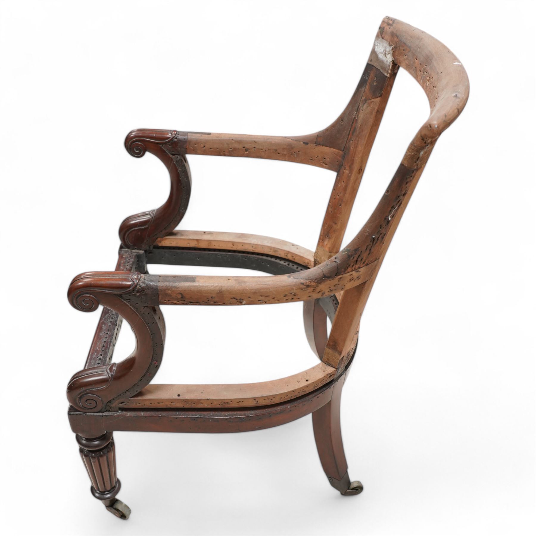 Regency mahogany and hardwood-framed library chair, curved and rolled cresting rail over scroll and lappet carved arm terminals, on turned and reed carved supports with brass castors 