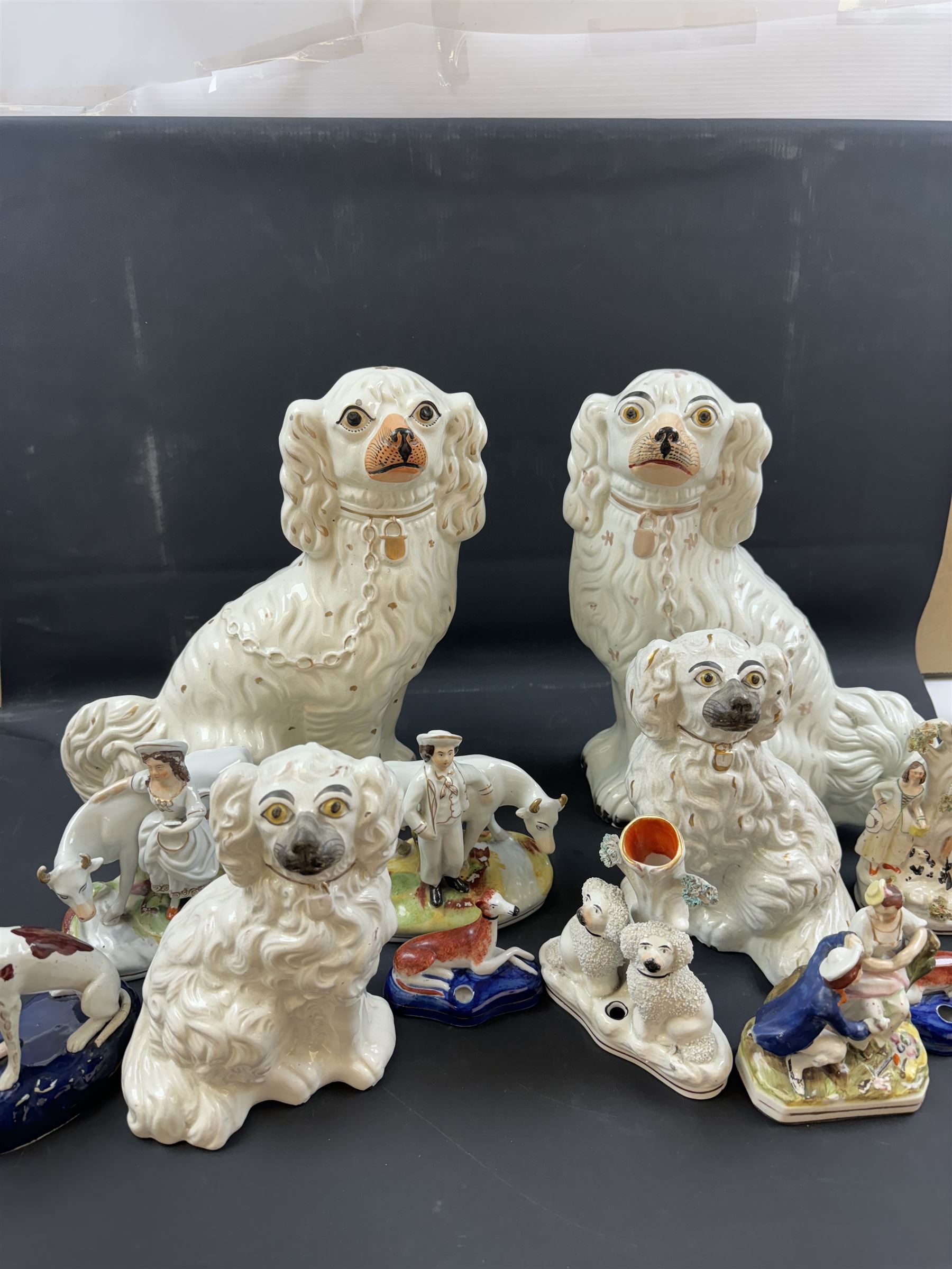 Staffordshire and Staffordshire style figures, to include a chained hound upon a blue oval base in the manner of Samuel Alcock, two pairs of seated Spaniels, a pair modelled as male figure and milk maid with cows, pair of recumbent Greyhounds, etc.