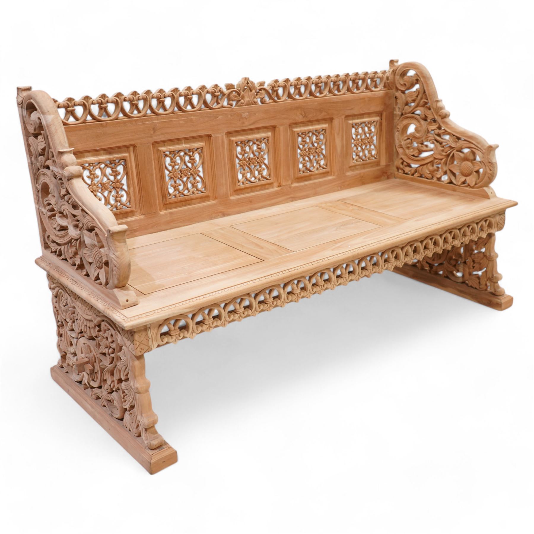 Hand carved teak garden bench, C-scroll and foliate carved cresting rail over four pierced and flower head carved panels, shaped and scrolling end supports carved with flower heads and curling leafy branches, united by pegged stretcher