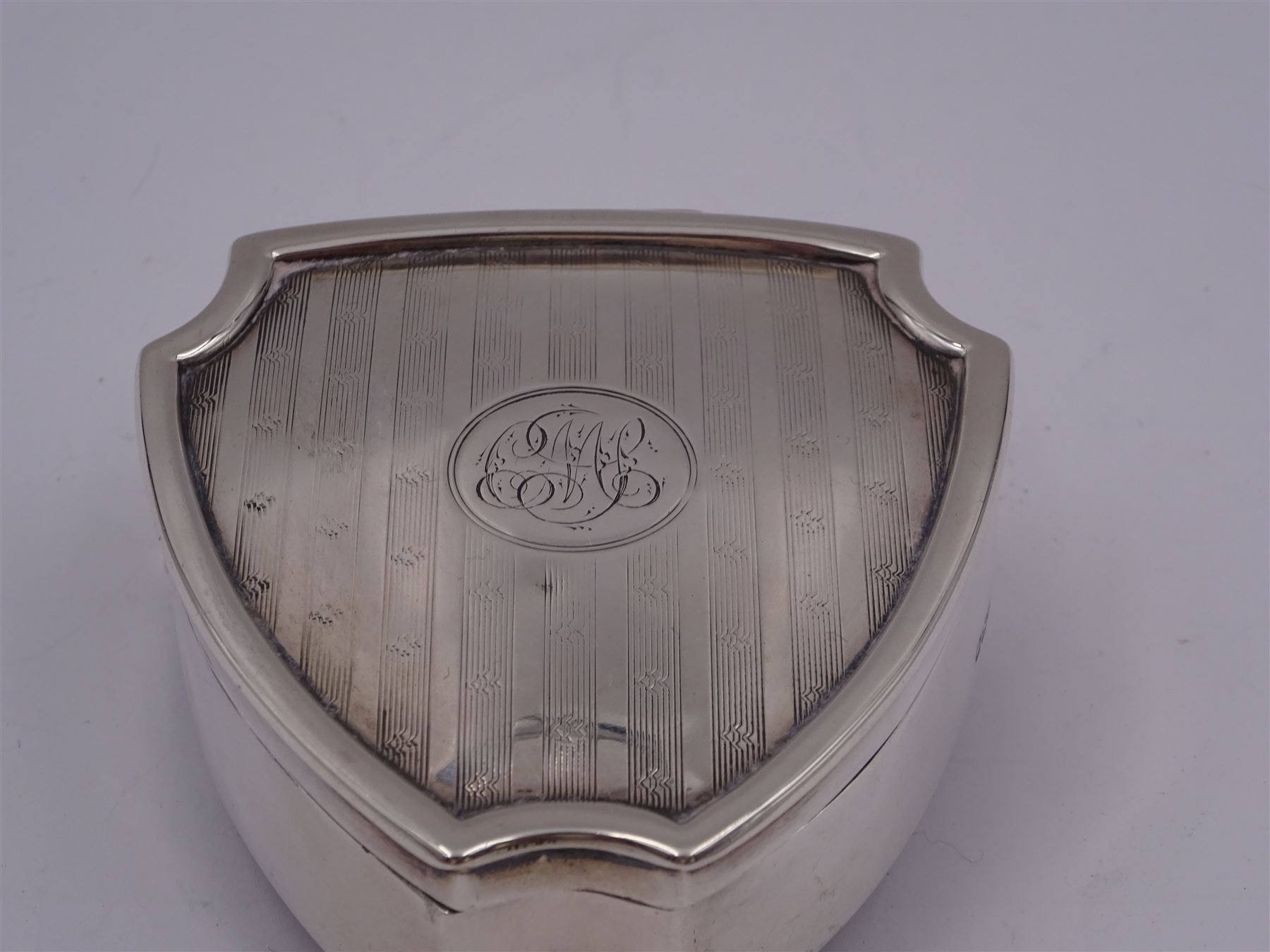 Early 20th century silver mounted trinket box, of shield form, with engine turned decoration and engraved circular cartouche to hinged cover, opening to reveal green velvet interior, upon three pad feet, hallmarked Walker & Hall, Sheffield 1914, H3.5cm, W7cm