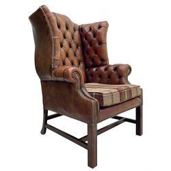 Georgian design hardwood-framed wingback armchair, shaped cresting rail and deep wingback over rolled arms, upholstered in brown buttoned leather with studwork bands, the seat cushion upholstered in checkered fabric, on square supports united by stretchers (W86cm, H118cm, D86cm); together with matching rectangular footstool (63cm x 43cm, H37cm) 