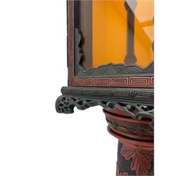 20th century Chinese black and red lacquered hardwood lantern stand, hexagonal shaped canopy top carved with flower heads and scrolls, the lantern fitted with amber tinted glass panes, pierced and carved upper panels, enclosed by two hinged doors, turned stem carved in relief with trailing vine leaves with fruits, stepped hexagonal base with carved decoration  