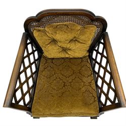 Early 20th century three-piece bergère suite - three seat sofa (W177cm, H82cm, D75cm); pair of matching armchairs (W84cm); single caned back with 'cock-pen' panelled arms, upholstered in foliate pattern fabric, blind fretwork lower frieze over square feet 