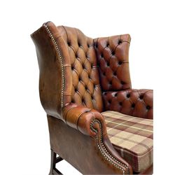 Georgian design hardwood-framed wingback armchair, shaped cresting rail and deep wingback over rolled arms, upholstered in brown buttoned leather with studwork bands, the seat cushion upholstered in checkered fabric, on square supports united by stretchers (W86cm, H118cm, D86cm); together with matching rectangular footstool (63cm x 43cm, H37cm) 