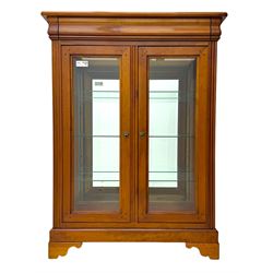 20th century cherry wood display cabinet, projecting cornice over two glazed doors with bevelled panes flanked by fluted support columns, enclosing three adjustable glass shelves with mirror-back surface, supported by shaped bracket feet