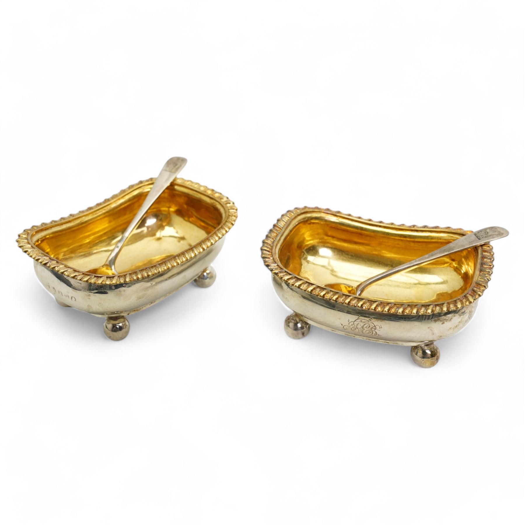 Pair of George III silver salts of elongated oval design with gilded interior and gadrooned border engraved with a monogram, raised on ball feet each 8.5cm x 6cm London 1820 Maker Rebecca Emes and Edward Barnard I together with a pair of later salt spoons