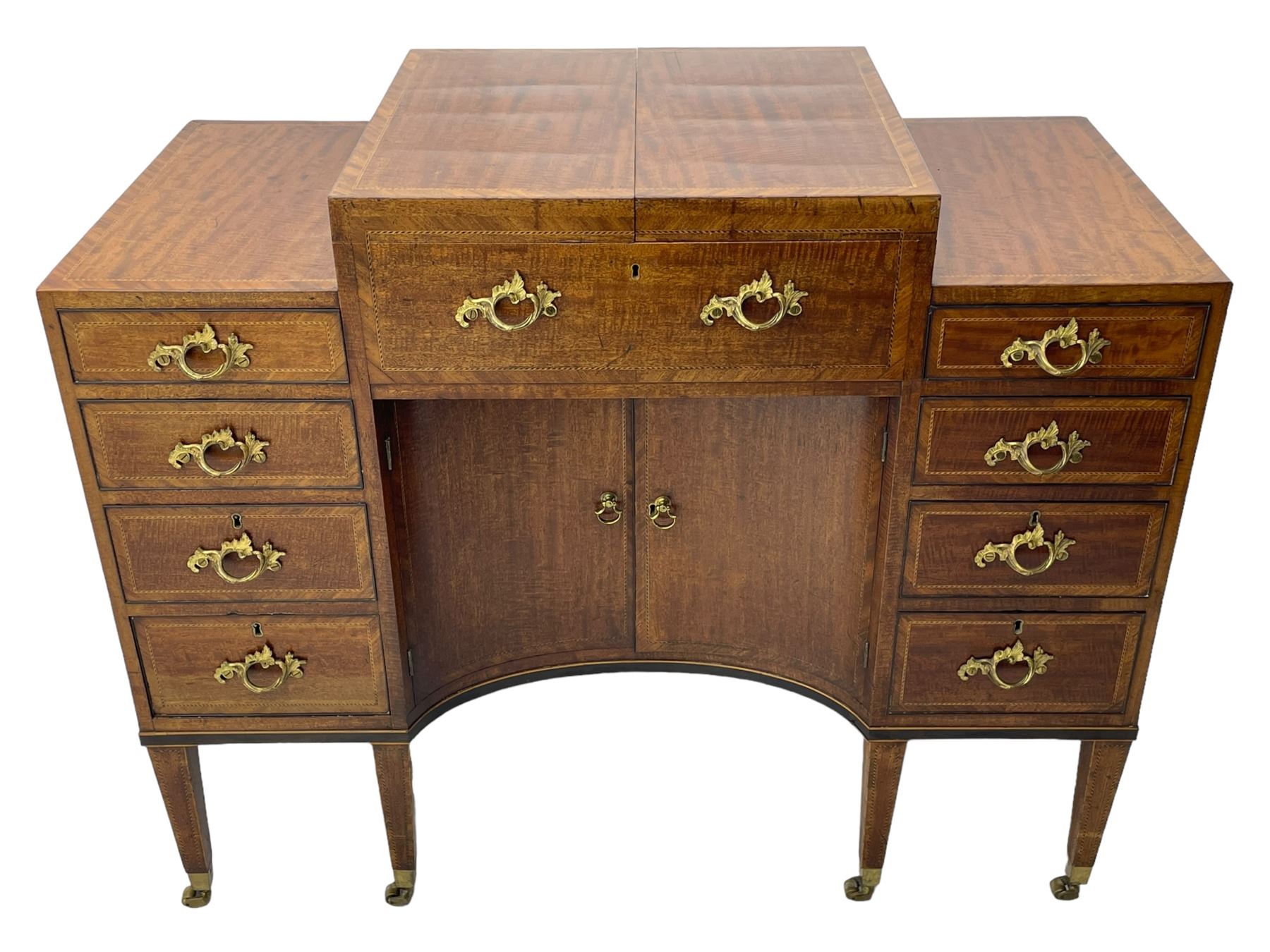 Late 19th century mahogany and satinwood dressing chest, the raised middle section hinges to reveal an interior fitted with lidded compartments, removable tray, single drawer and glass scent bottles, lift-up bevelled mirror with adjustable hinged mechanism, fitted with a further eight cock-beaded graduating drawers and curved kneehole with double cupboard, square tapering supports on brass cups and castors, inlaid throughout with checkered stringing, ornate Rococo cast gilt metal handles