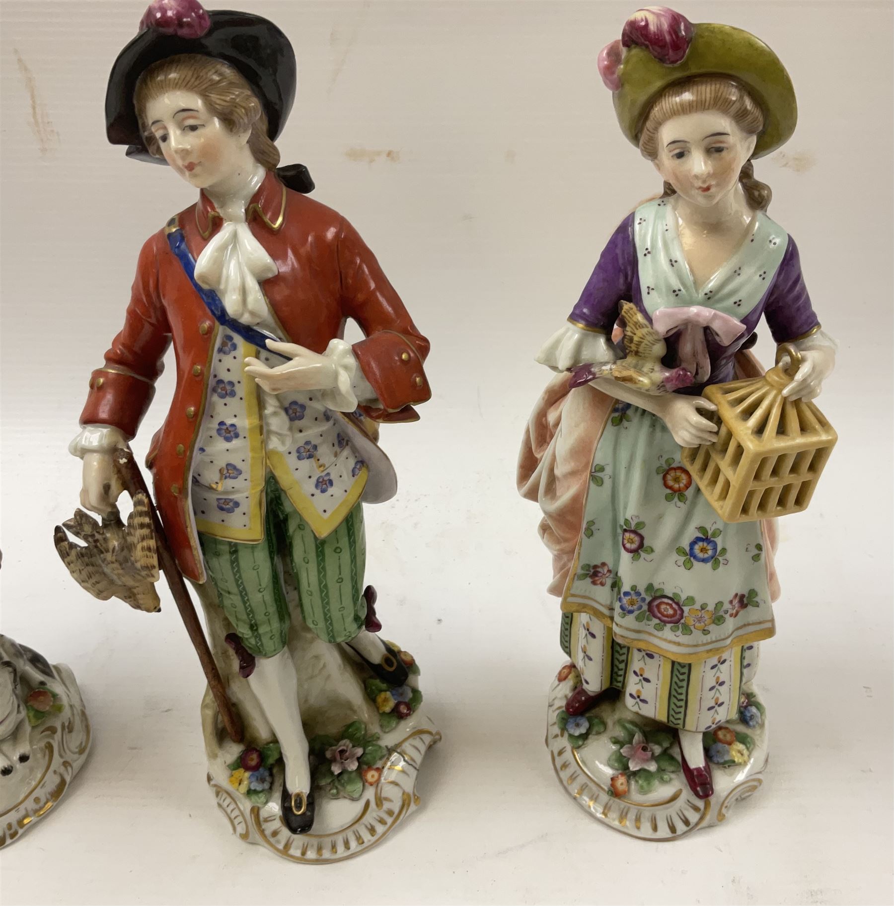 Pair of Naples figures, she holding bird cage with bird perched upon her arm, he holding game, each approximately H23cm, together with a Sitzendorf figure modelled as a figure with wine glass and bottle, with dog laid at feet, H22cm