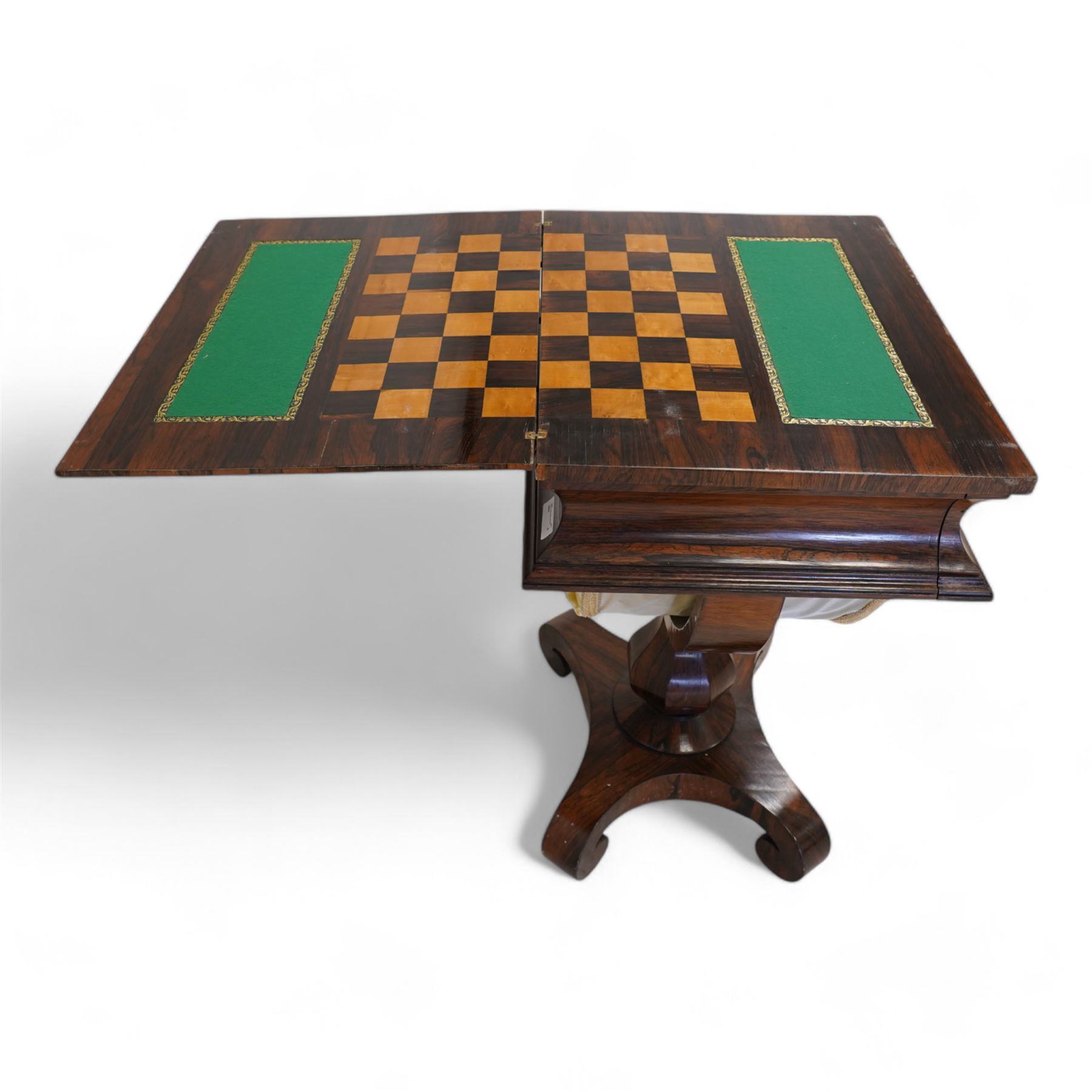 Regency rosewood games table, the rectangular swivel and fold-over chamfered top opening to reveal an inlaid checkerboard and baize lined playing surface, fitted with single concave frieze drawer over an upholstered sliding well fitted with compartments, supported with a U-shaped frame raised on an octagonal vasiform pedestal, terminating to a quadriform base with down-scrolled feet