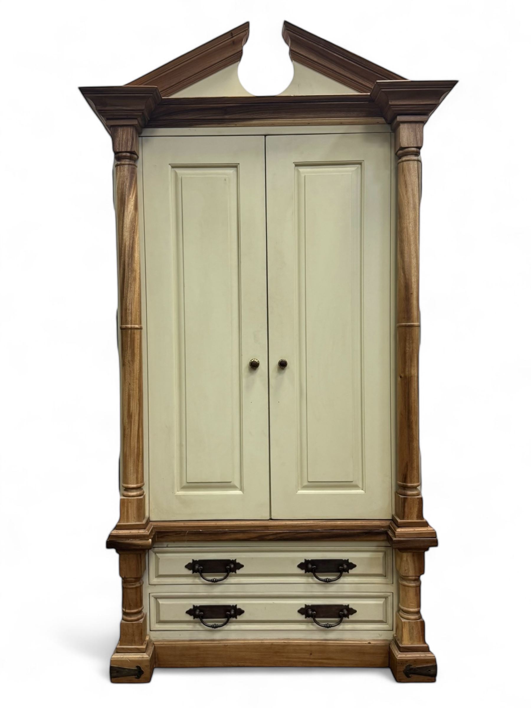 Hardwood and cream painted kitchen larder cupboard, sloped pediment over two panelled doors, the interior fitted with slides, drawers and storage shelves, two long drawers below, mounted by turned pilasters, on metal bound moulded plinth base