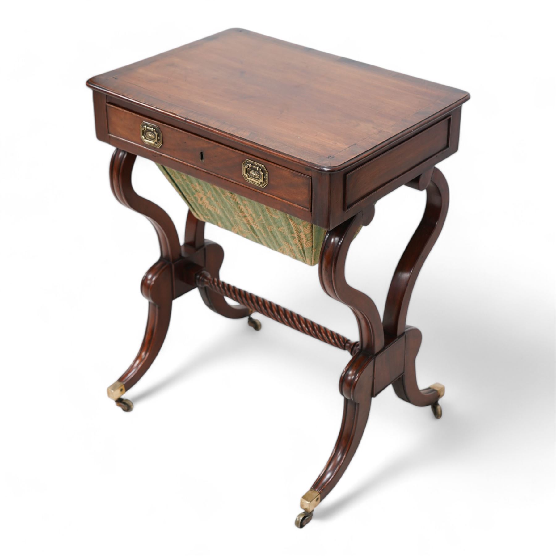 Regency mahogany work table, rectangular top with banded and moulded edge inlaid with checkered stringing, fitted with single cock-beaded drawer over upholstered sliding well, raised on scrolled twin end supports, united by a spiral-turned stretcher, on splayed supports with brass cups and castors