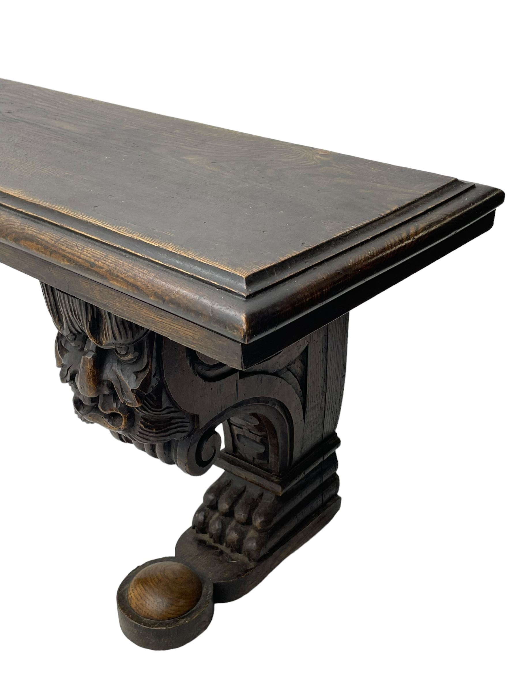 Victorian oak bench, moulded rectangular top, on mask and scroll carved corbel supports with paw feet, rectangular platforms with rounded terminals and applied roundel 