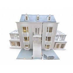 Large three storey modern dolls house, painted white with latticed windows, grey roof and metal fencing, with decorated interior, together with two dolls house garden rooms and two conservatories