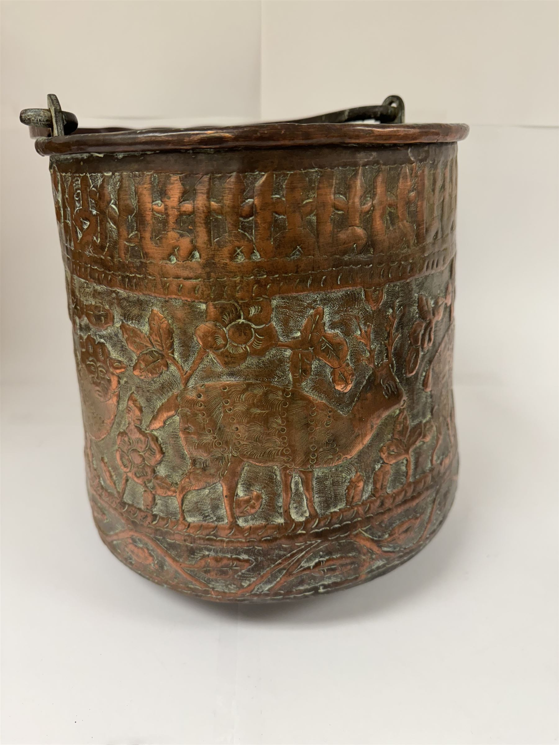 Middle eastern copper bucket, with chased and embossed band of animal decoration, together with a copper jardinière embossed with floral panels, copper plate with embossed leaf motif and two brass helmet shaped coal scuttles, bucket H26cm