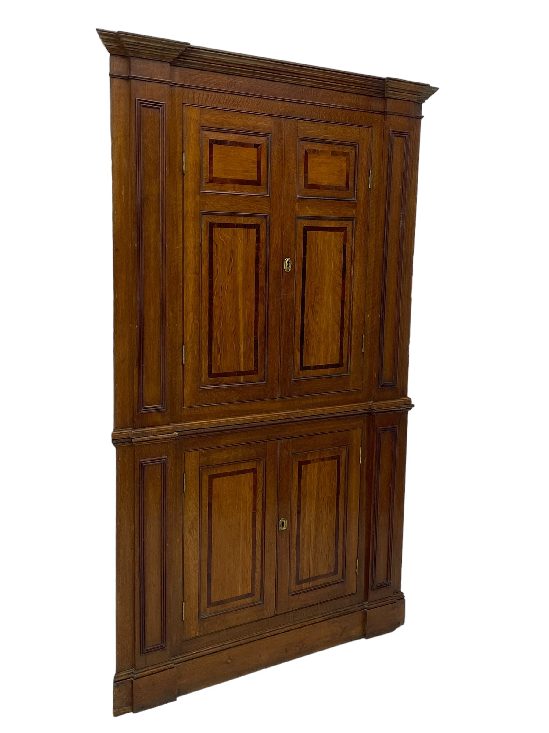 George III and later oak and mahogany banded corner cupboard, moulded cornice over four panelled doors, the door panels inlaid with mahogany bands, projecting square pilasters throughout with applied reeded mouldings, the painted interior fitted with shaped shelves, on moulded plinth base 