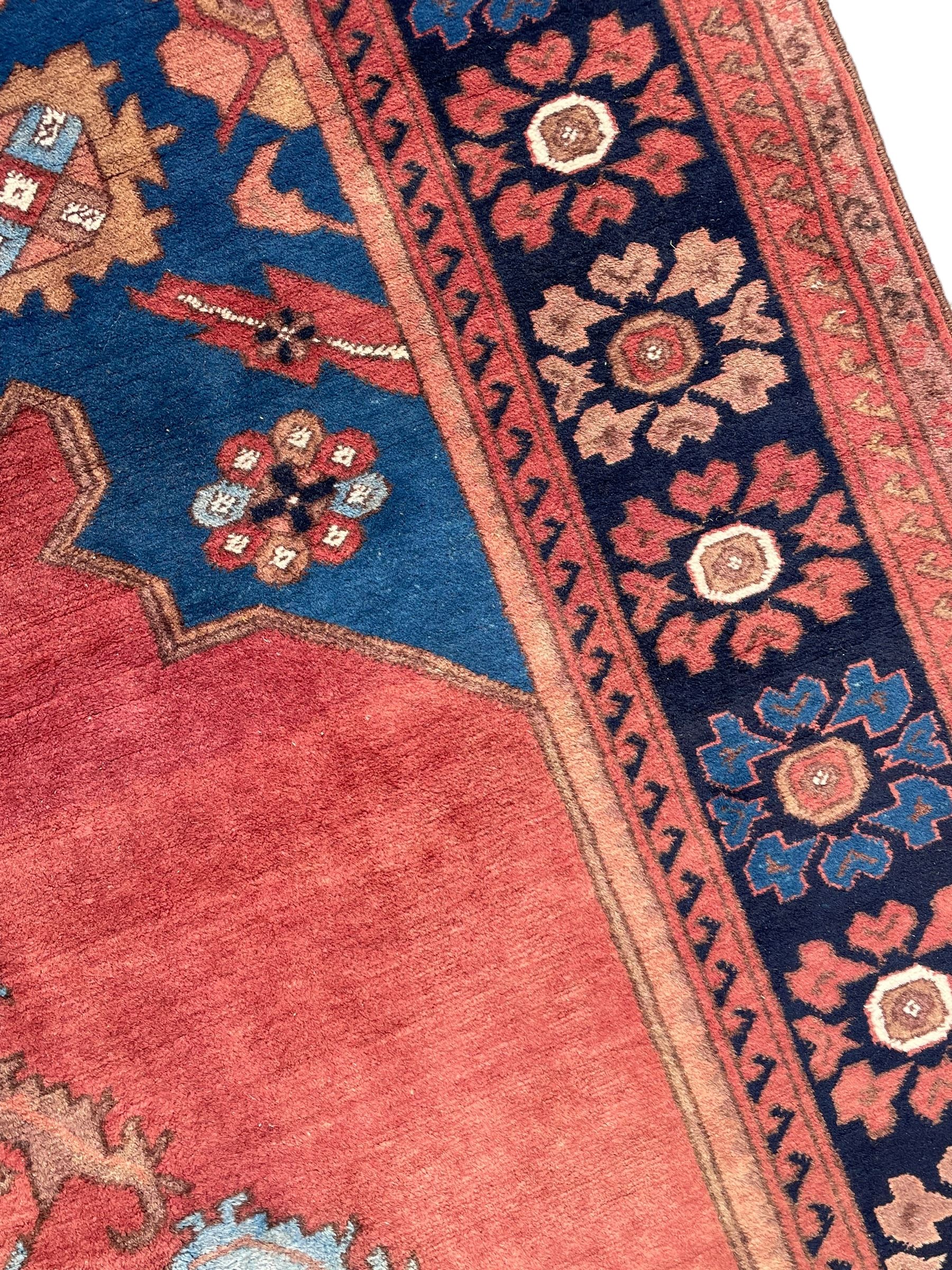 Afghan rust ground carpet, large central lozenge medallion decorated with stylised plant motifs, running water guard stripes enclosing indigo ground border decorated with stylised flower heads