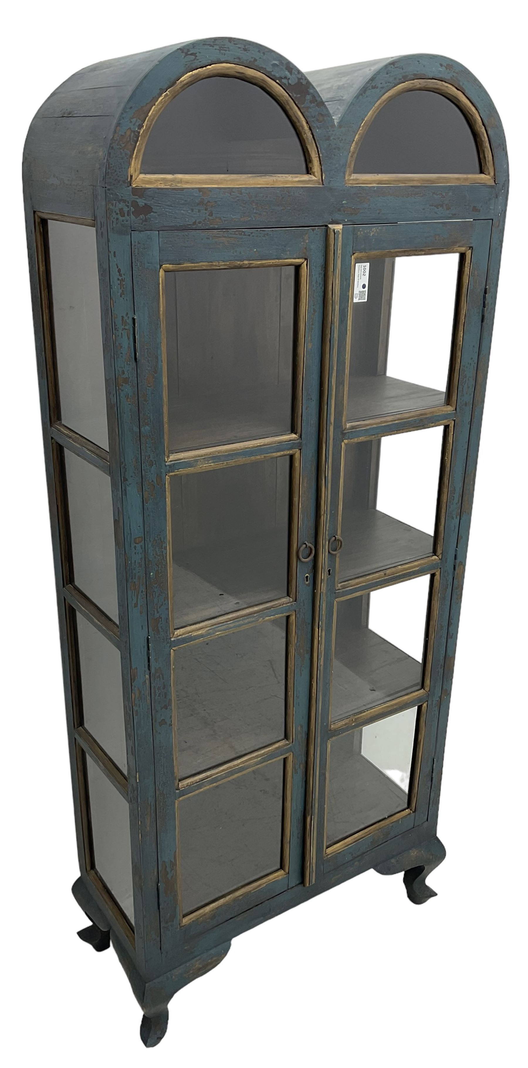 Tall painted glazed display cabinet, double arched top over two glazed doors, fitted with three shelves, in rustic blue paint finish, on cabriole feet