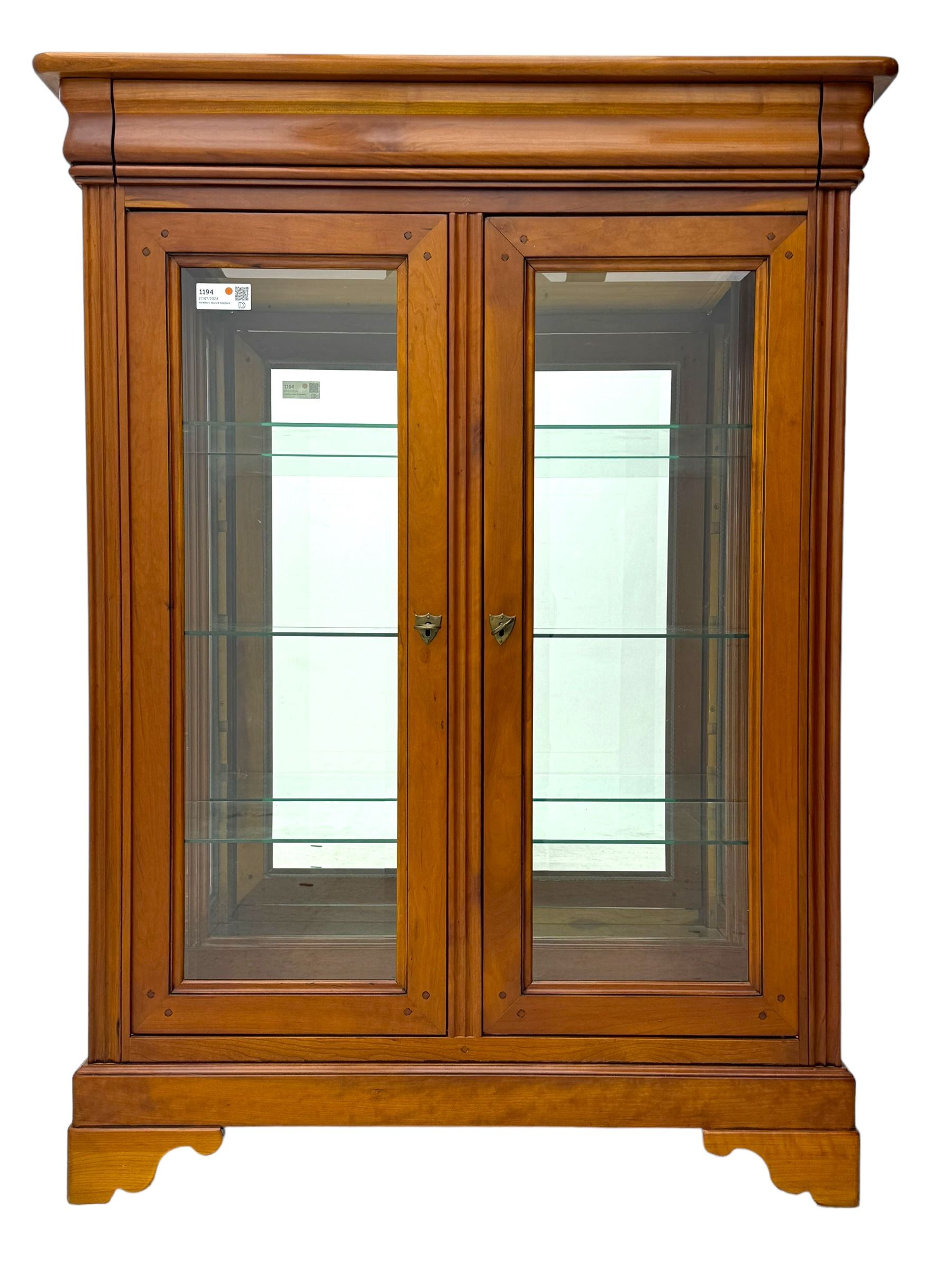 20th century cherry wood display cabinet, projecting cornice over two glazed doors with bevelled panes flanked by fluted support columns, enclosing three adjustable glass shelves with mirror-back surface, supported by shaped bracket feet