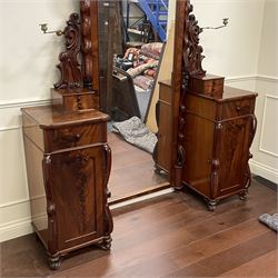 Tall Victorian figured mahogany twin pedestal dressing table, the tall mirror with flower head and scrolled leaf carved pediment, flanked by two turned and carved finials over faceted lancet arched lantern tops, plane mirror plate enclosed by shaped frame, pierced and undulating moulded uprights, on C-scroll and curled leaf carved supports fitted with cast brass hinged candle sconces, each pedestal fitted with two small trinket drawers over larger drawer and panelled cupboard, canted corners with matched upright mounts, the cupboard doors enclosing slides, on scroll carved feet 