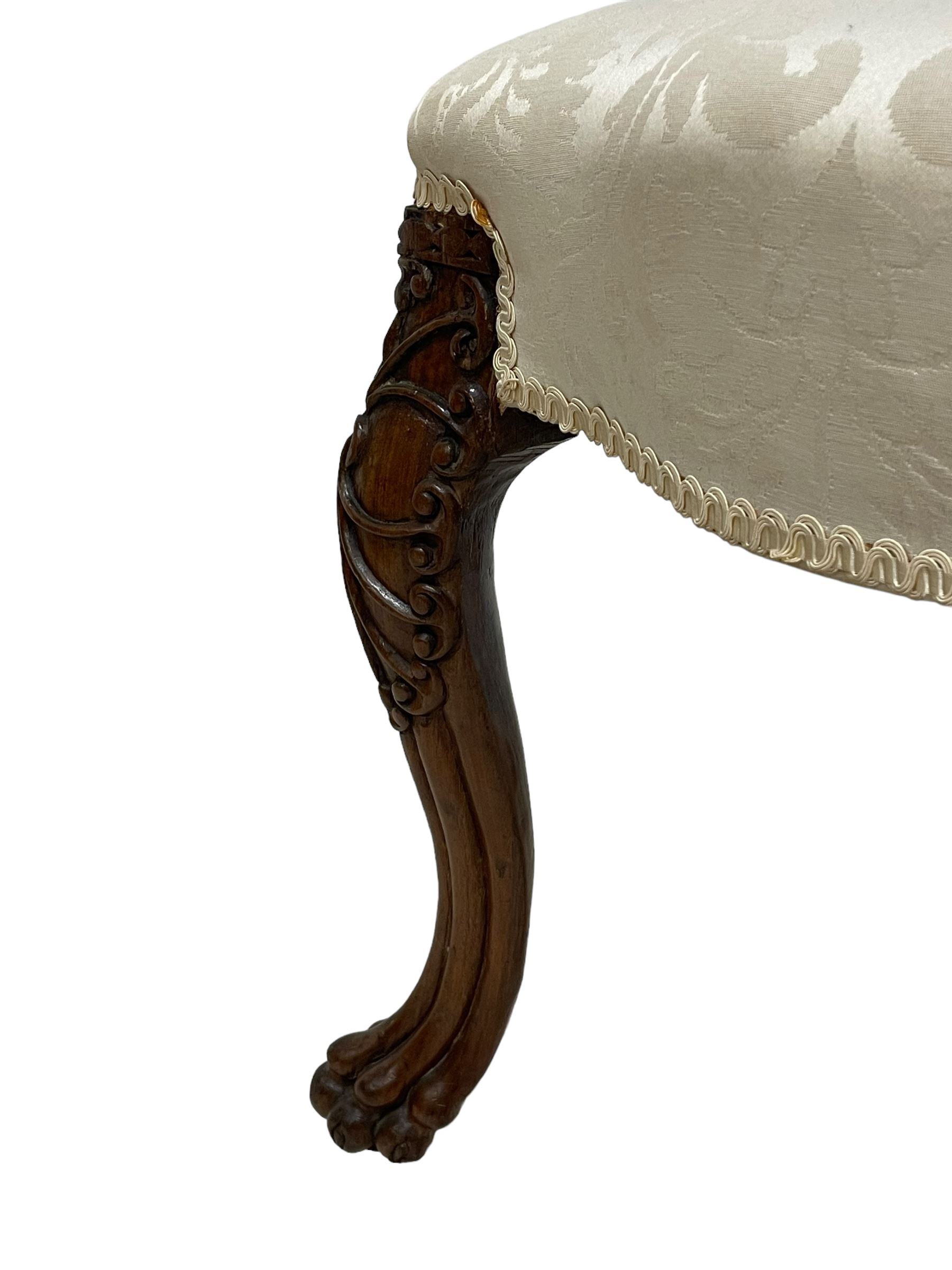 Georgian Irish mahogany dressing stool, overstuffed seat upholstered in in ivory damask fabric, the cabriole supports decorated with moulded interlacing scroll motifs with mycelium cap detail, over lobe carvings terminating to large paw feet