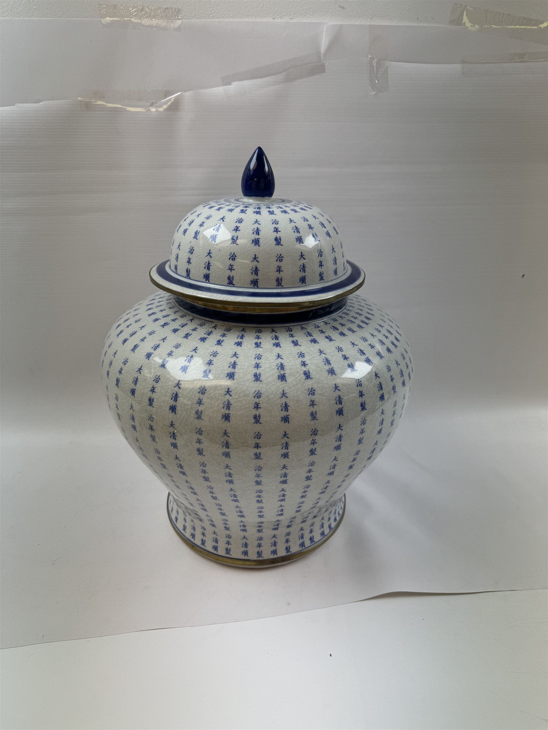 Large Oriental design ginger jar and cover, of squat baluster form with domed cover, decorated in blue with Chinese characters against a white crackle glaze ground, the cover, neck and foot rim with applied brass band, with character mark beneath, H43cm