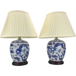 Pair of blue and white ovoid form table lamps, each decorated with dragons chasing the flaming pearl amidst clouds, raised upon circular hardwood bases, H28cm excluding fitting