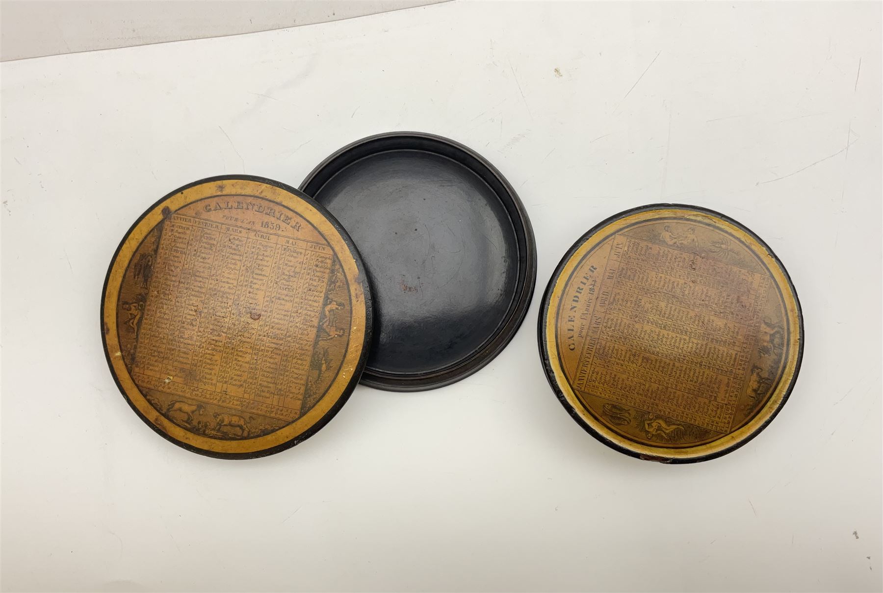 Two 19th century French papier-mâché snuff boxes, each of circular form decorated with the French calendar and detailed 'Calendrier pour l'an 1839' and 'Calendrier pour l'annee 1844' to top and ''Saisons' to base, further detailed with the months, days and additional notations alongside symbols from the zodiac, larger example D9.5cm, smaller example D8.5cm