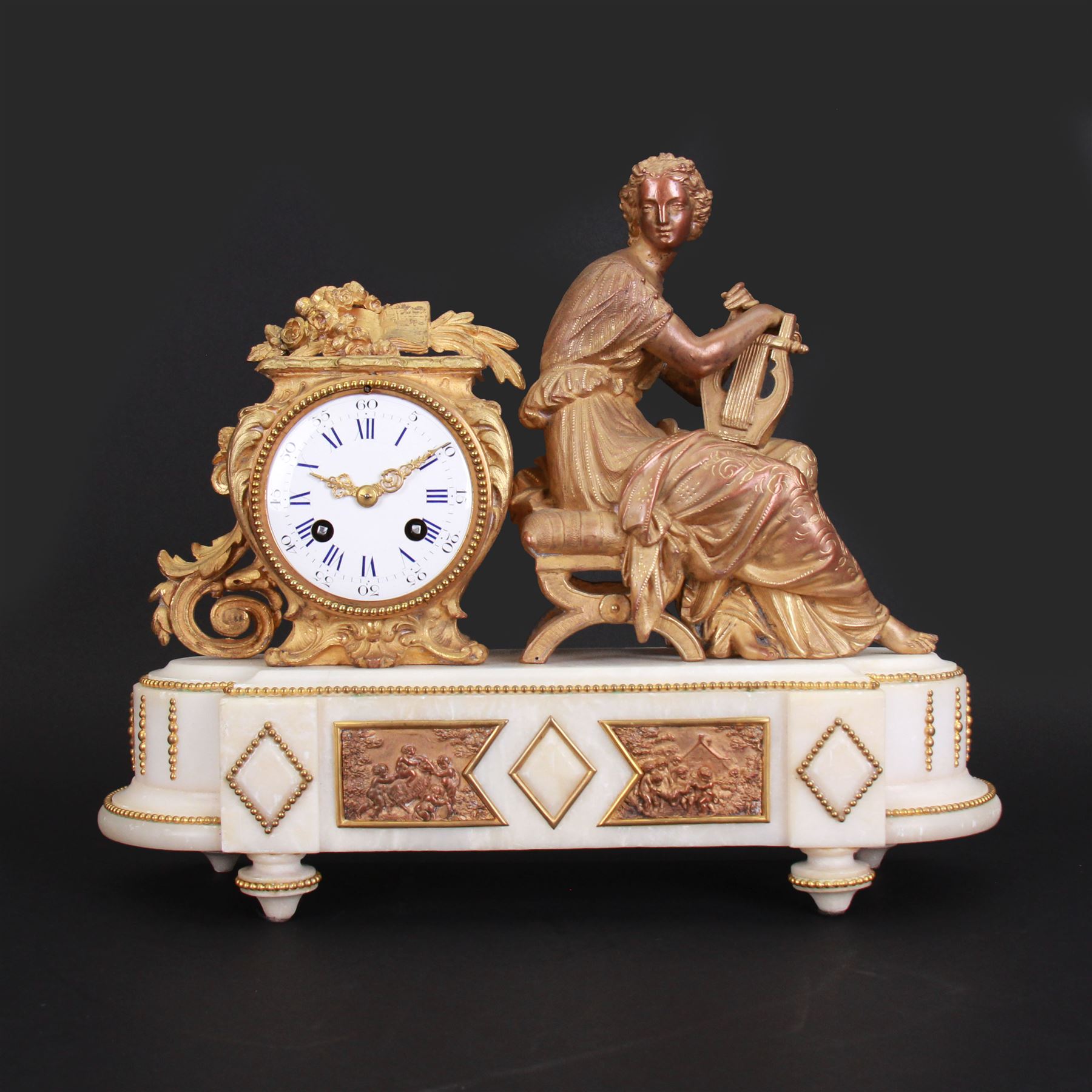 French - late 19th century 8-day figural mantle clock c 1880, with a breakfront alabaster plinth raised on four conforming feet, with two recessed and three raised lozenge panels, continuous bead decoration and a cast gilt figure of a seated female playing a Lyre,  Parisian drum movement with an enamel dial and Roman numerals, five-minute Arabic's and gilt Louis XVI hands, twin train countwheel striking movement, striking the hours and half-hours on a bell. With Pendulum. 