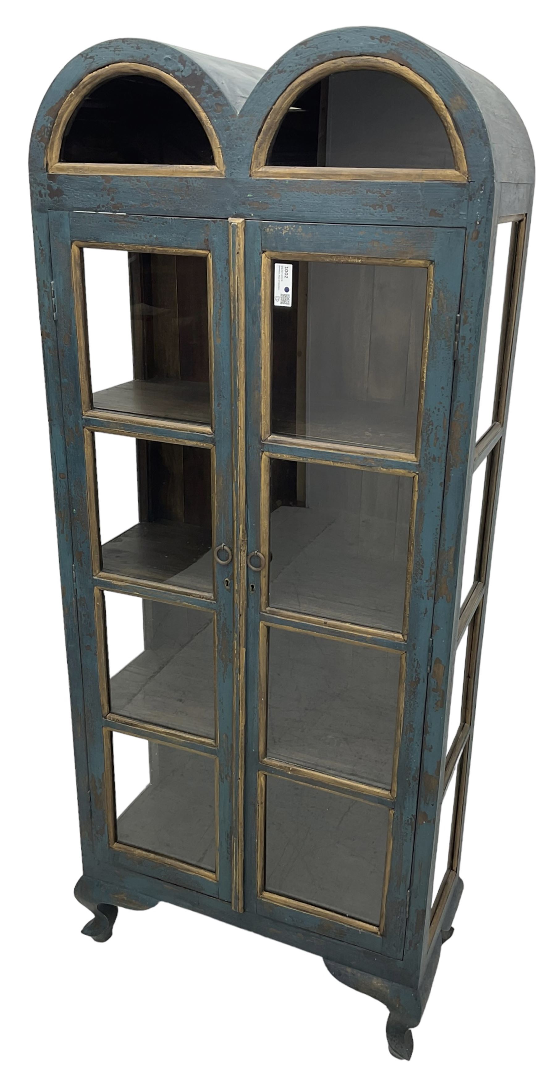 Tall painted glazed display cabinet, double arched top over two glazed doors, fitted with three shelves, in rustic blue paint finish, on cabriole feet