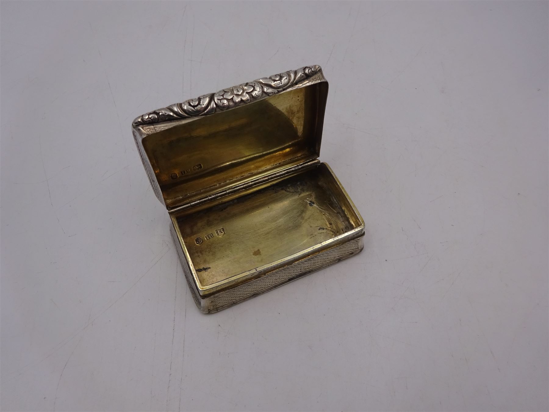 George IV silver snuff box, of rectangular form, with engine turned decoration, chased foliate borders and blank cartouche to centre of hinged cover, opening to reveal a gilt interior, hallmarked John Bettridge, Birmingham 1825, W7.6cm