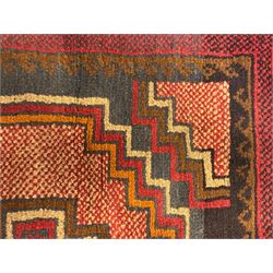 Baluchi crimson ground rug, the central field decorated with two stacked geometric lozenge medallions, surrounded by stepped multicoloured motifs, the wide border with alternating angular motifs in deep red, within a narrow brown guard stripe