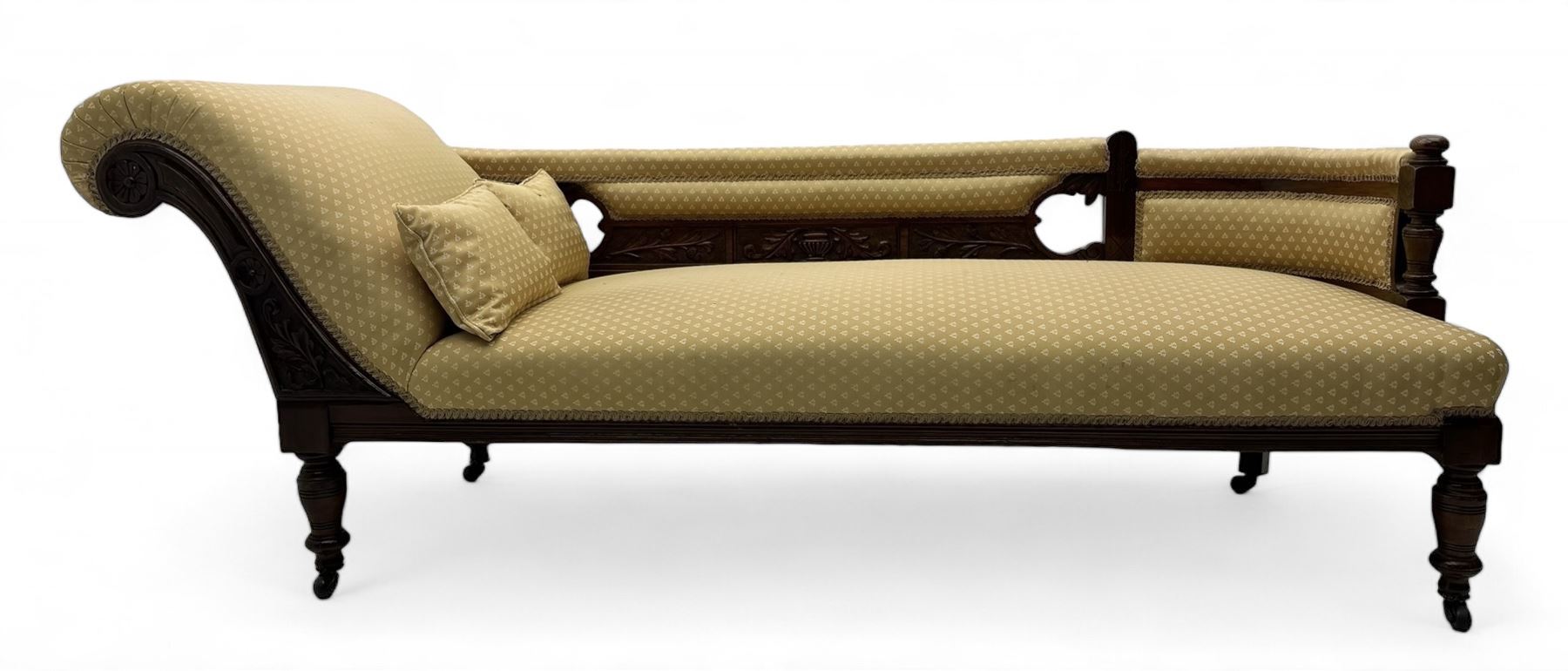 Late Victorian walnut framed chaise longue, scrolled backrest and sides upholstered in patterned yellow fabric, carved floral motifs to the backrest and sides, raised on turned supports with castors