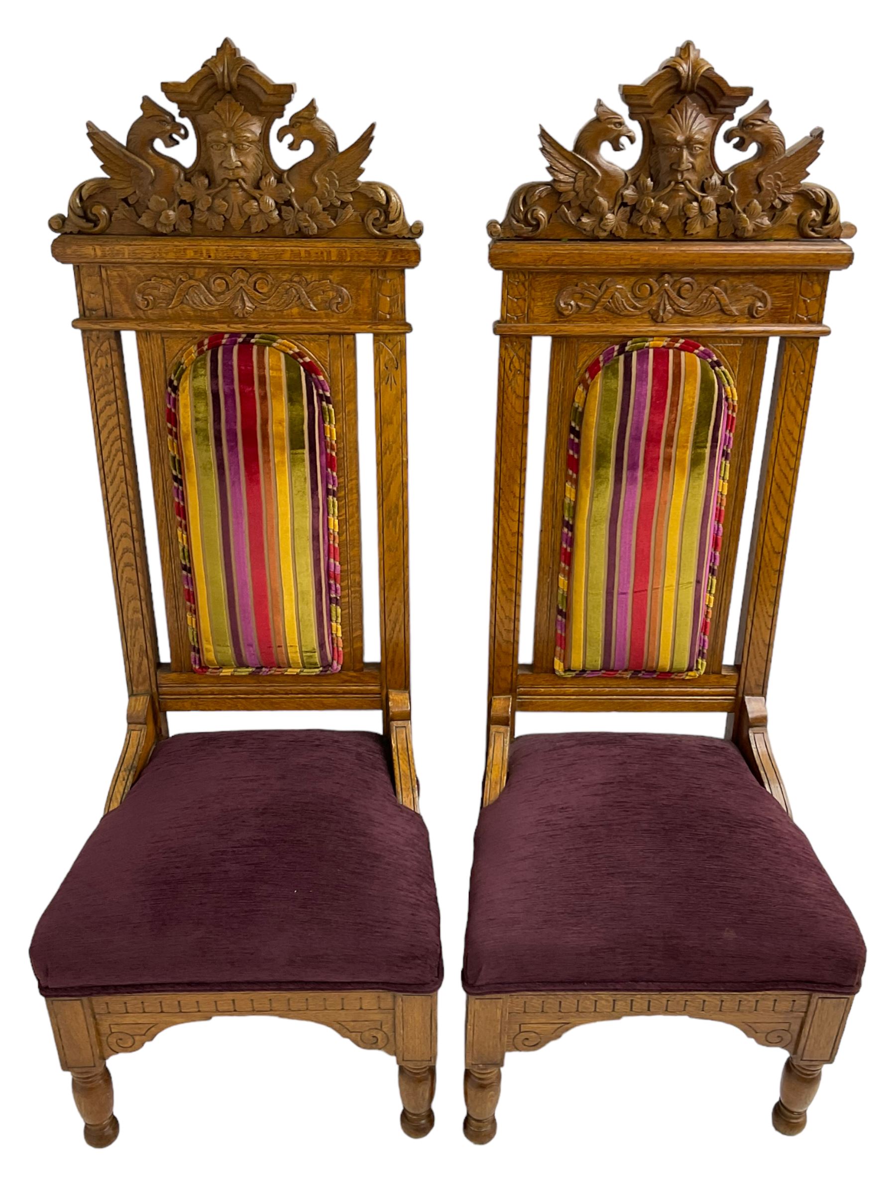 Set of six 20th century Carolean design oak high back chairs, the pediment carved with dragons and central Green Man mask with trailing foliage, the backs upholstered in striped fabric, on turned front supports