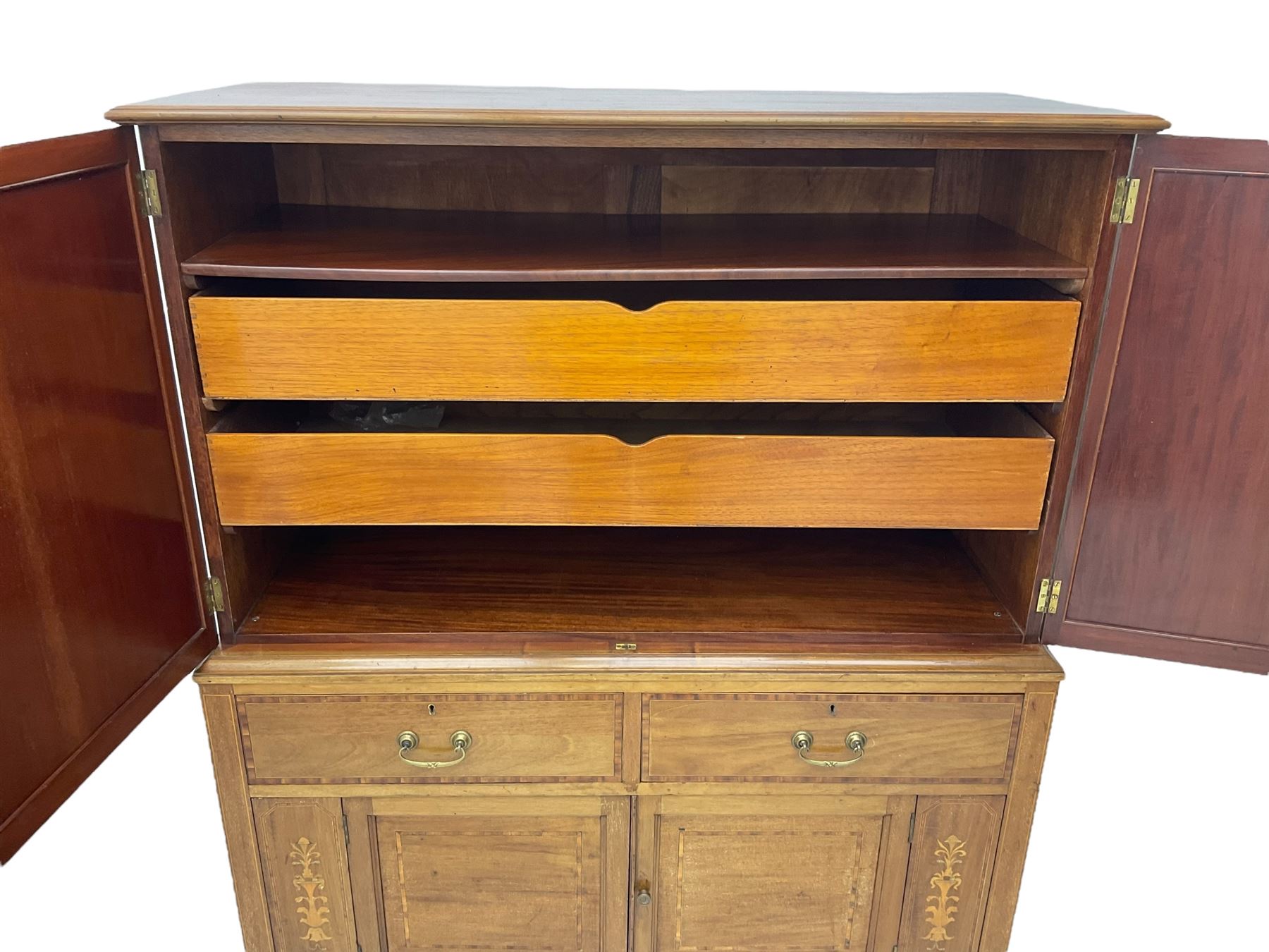 Early 20th century inlaid mahogany cabinet, two-door upper section revealing interior shelving and two large pull-out drawers, the lower section comprises two wide drawers flanked by inlaid floral motif panels above a double-door cupboard, supported by tapering legs with brass castors