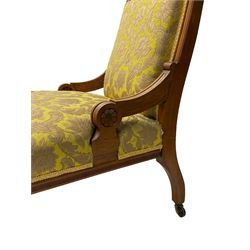 Late Victorian oak nursing chair, moulded frame with flower head carved roundels, upholstered in floral pattern fabric, on turned front feet with brass and ceramic castors 