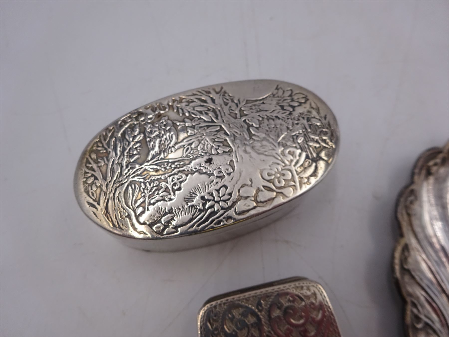 Modern silver oval box, decorated to the removable cover with an owl on a branch, hallmarked London 1984, makers mark KB, together with a modern silver pin tray of scrolling lobed form, hallmarked 1992, makers mark EM, and an early 20th century silver pill box, hallmarked Adie & Lovekin Ltd, Birmingham 1910, oval box H2.2cm, W6.5cm