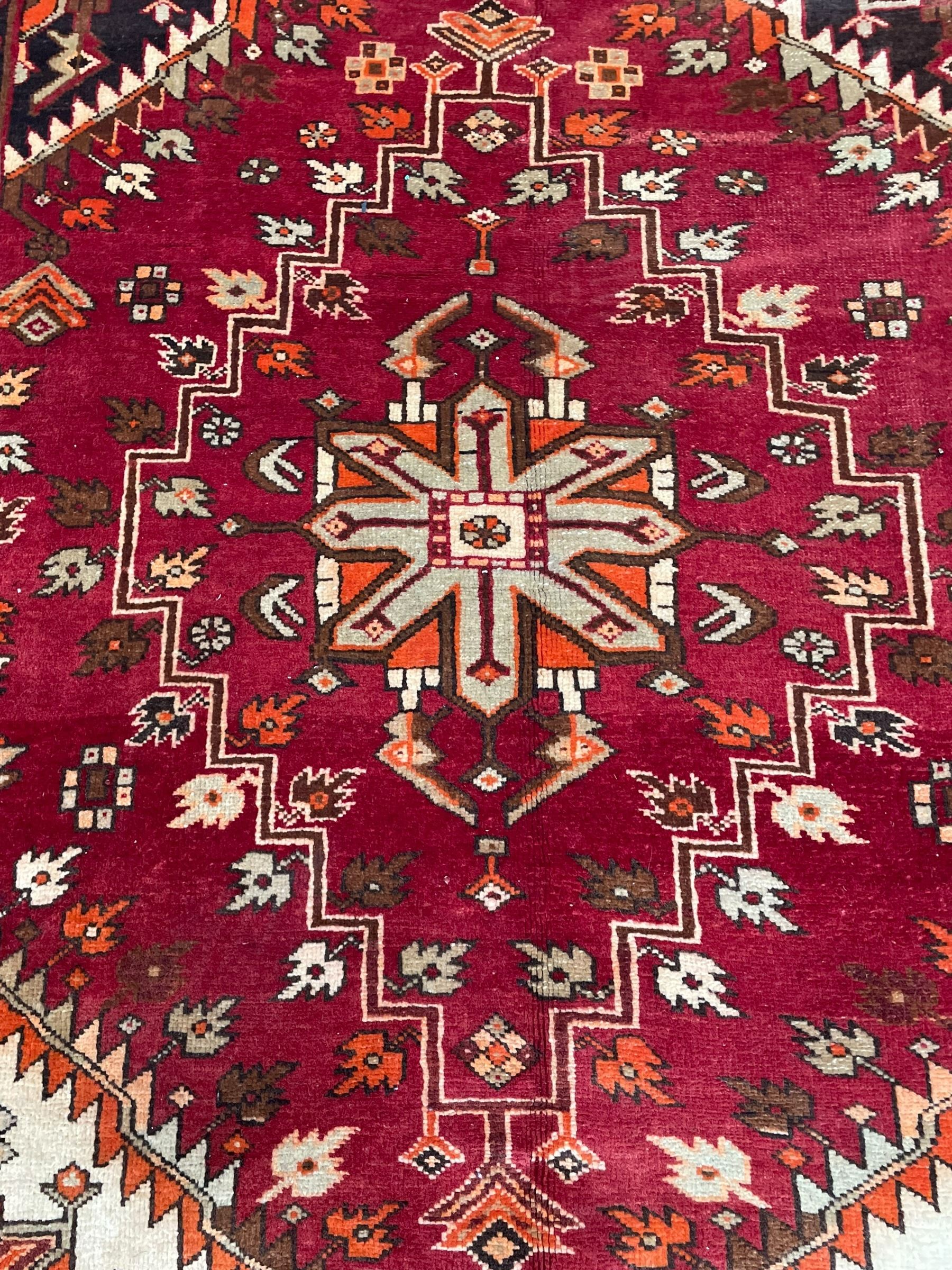 Persian crimson ground rug, the field decorated with three medallions within stepped borders, decorated all over with small stylised plant motifs, trailing flower head outer band and floral pattern border 