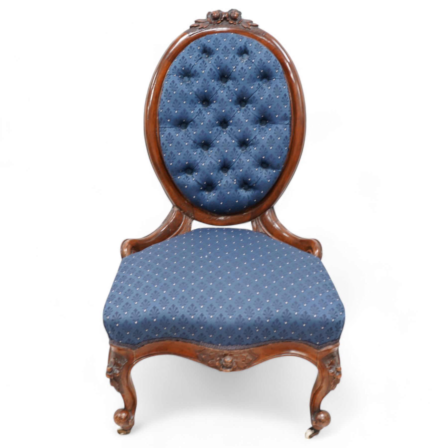 Victorian carved walnut framed nursing chair, the cresting carved with flower heads and extending foliage, upholstered in buttoned blue fabric with repeating pattern, on floral carved cabriole feet