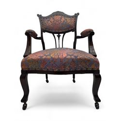 Late Victorian mahogany framed armchair, upholstered in muted purple fabric with iridescent floral pattern and nailhead trim, central foliate carved splat over padded scrolled arms, on cabriole supports fitted with castors