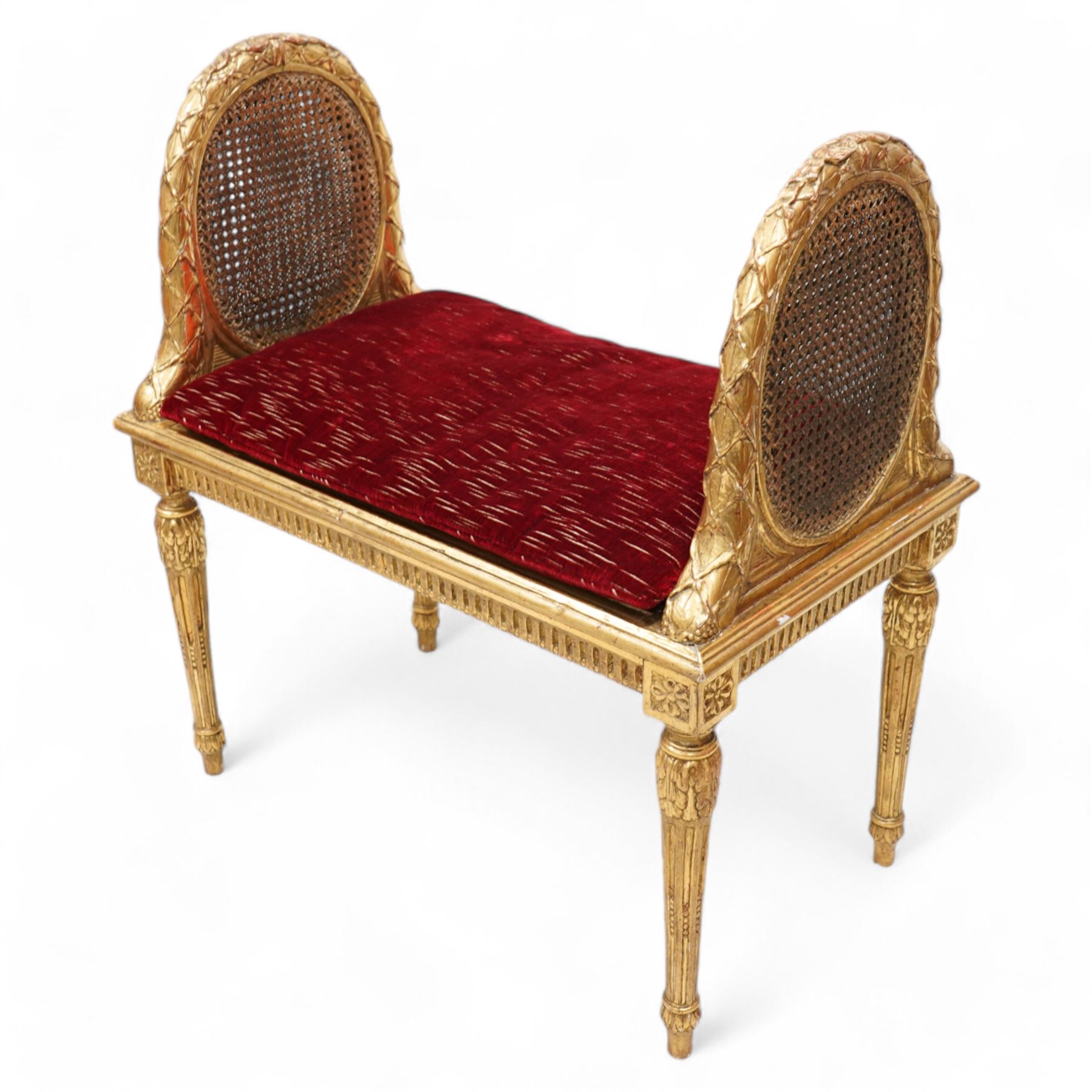 Late 19th century gilt wood and gesso window seat, raised oval cane work sides with lattice and ribbon decorated frame, rectangular cane work seat with upholstered squab cushion, moulded edge over fluted seat rails, on acanthus carved and stop-fluted turned supports 