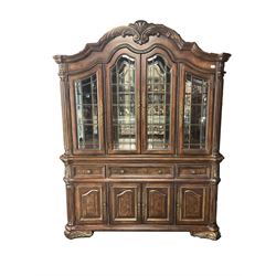 Kevin Charles American walnut display cabinet, illuminated interior, shell carved pediment above four bevel edge doors enclosing six glazed shelves above one central long drawer flanked by two short drawers, above three cupboards, carved bracket supports 