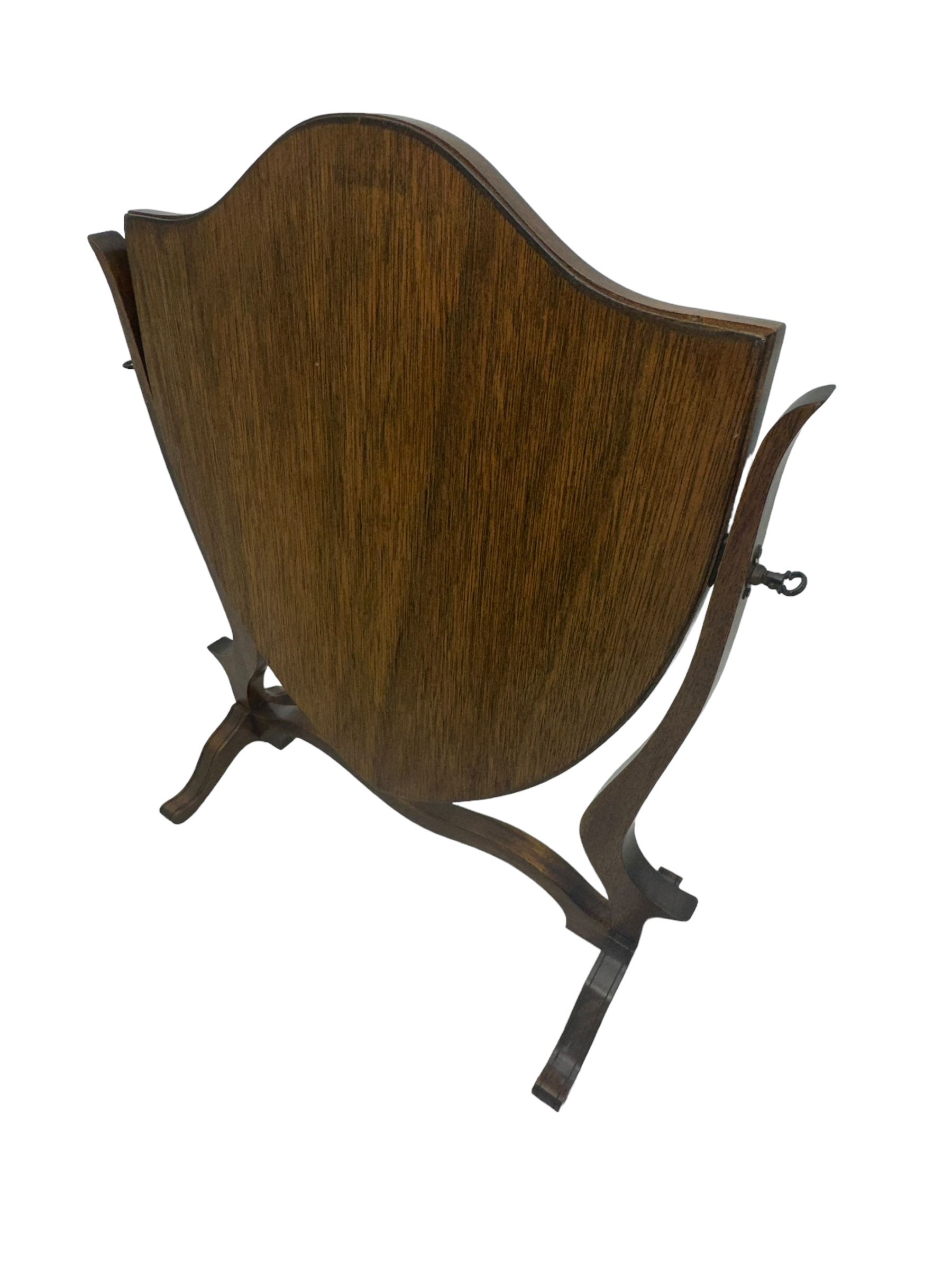 Edwardian mahogany shield-shaped dressing mirror, shaped frame with swivel function, on scroll supports connected by curved stretcher 