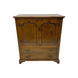 Oak drinks or media cabinet, projecting moulded cornice over two Gothic arch panelled doors on sliding tracks enclosing open storage, two drawers with brass drop handles, on bracket supports