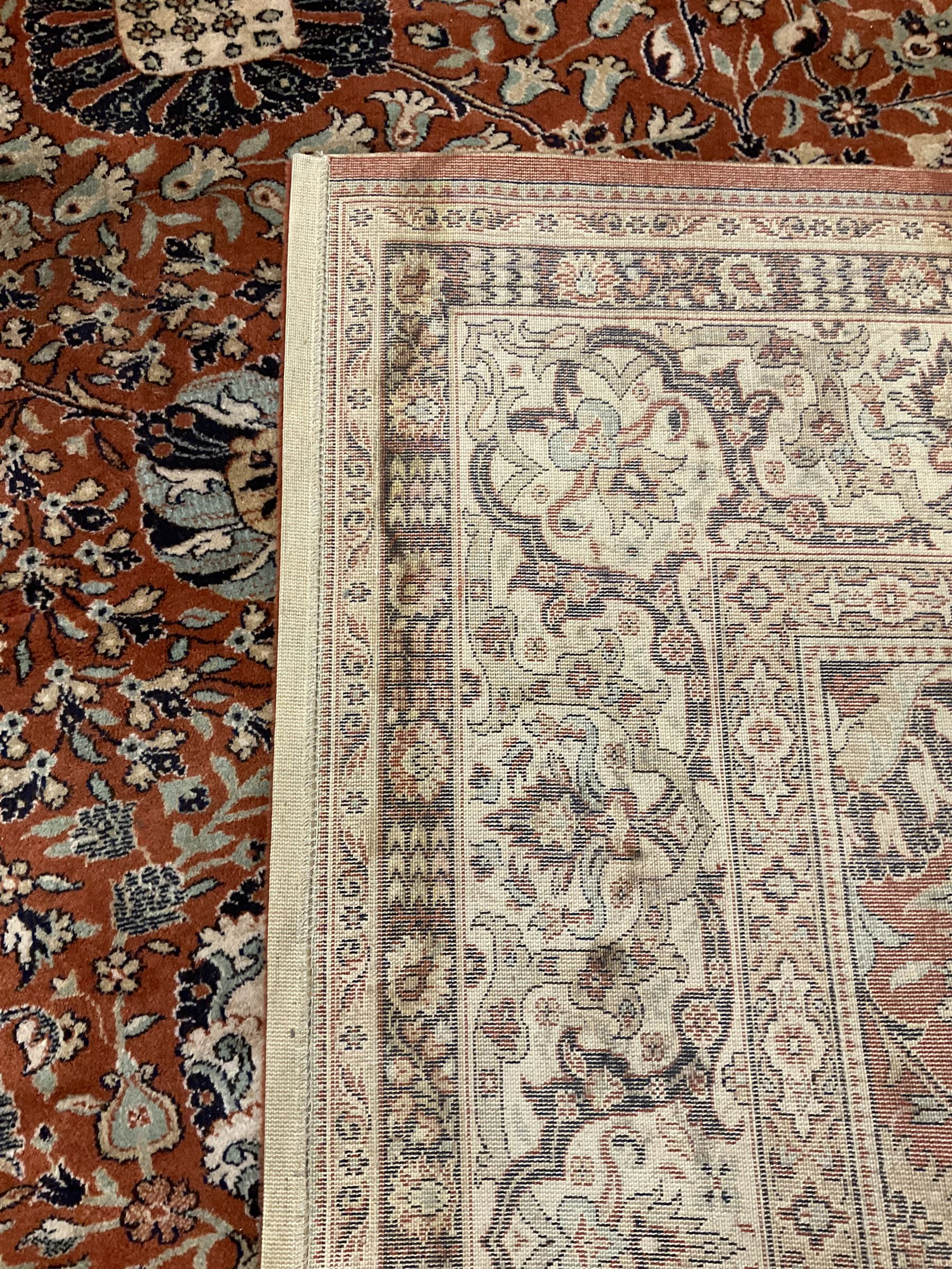 Persian design carpet, rust ground field decorated with large stylised plant motifs surrounded by smaller floral motifs, repeating trailing border