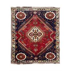 Persian Quashqai crimson ground rug, central geometric lozenge medallion surrounded by stylised plant motifs, indigo spandrels with further geometric designs, enclosed by an ivory border