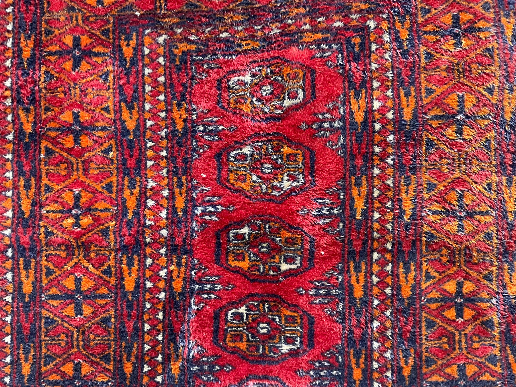 Persian Bokhara dark amber round rug, crimson field with six Gul motifs, surrounded by a guarded border with geometric design (124cm x 70cm); together with another similar in amber and red (101cm x 63cm) (2)