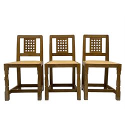 Mouseman - set of six oak dining chairs, pierced and carved lattice panel back over tan leather seat with studded band, on octagonal front supports united by plain H stretchers, carved with mouse signature, by the workshop of Robert Thompson, Kilburn 